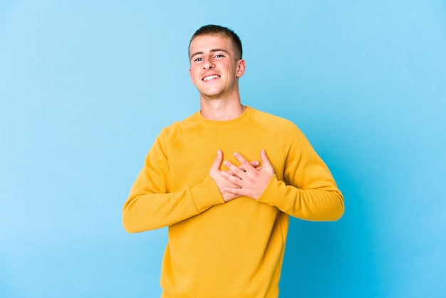 Joven guapo caucásico tiene expresión amistosa, presionando la palma contra el pecho. Concepto de amor.