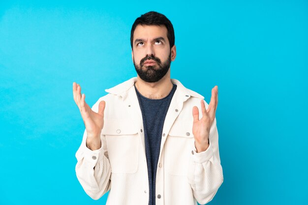 Joven guapo con chaqueta de pana blanca sobre pared azul aislado frustrado por una mala situación