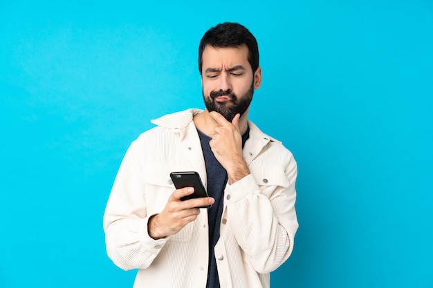 Joven guapo con chaqueta de pana blanca sobre pared azul aislado pensando y enviando un mensaje