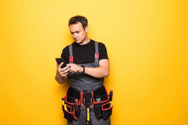 Joven guapo con cinturón de herramientas utiliza teléfono móvil