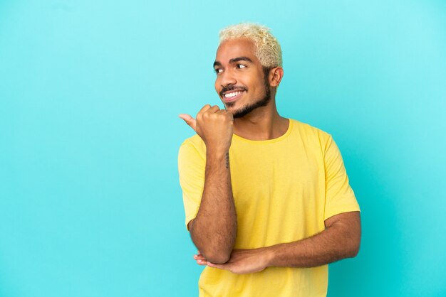 Joven guapo colombiano aislado sobre fondo azul apuntando hacia el lado para presentar un producto