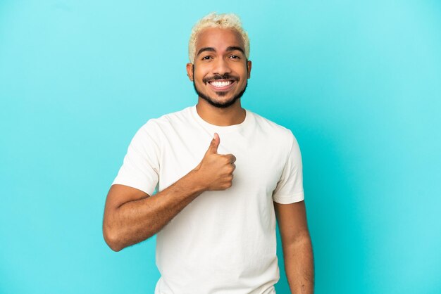 Joven guapo colombiano aislado sobre fondo azul dando un pulgar hacia arriba gesto