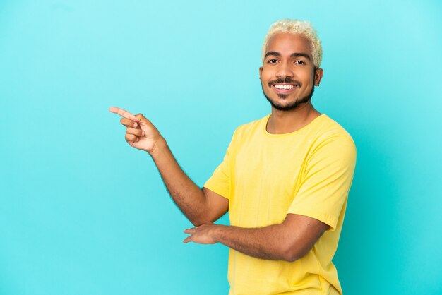 Joven guapo colombiano aislado sobre fondo azul dedo acusador hacia el lado