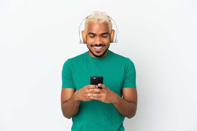 Joven guapo colombiano aislado sobre fondo blanco escuchando música y mirando al móvil