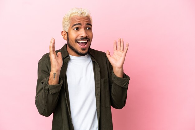 Joven guapo colombiano aislado sobre fondo rosa con expresión facial sorpresa