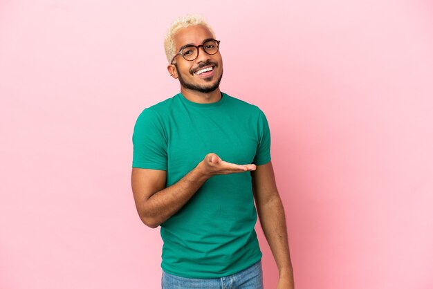 Joven guapo colombiano aislado sobre fondo rosa presentando una idea mientras mira sonriendo hacia