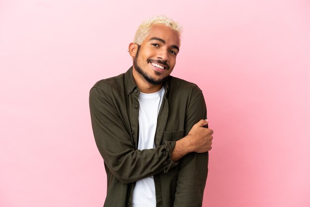 Joven guapo colombiano aislado sobre fondo rosa riendo