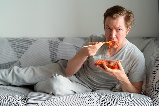 Joven guapo comiendo kimchi en la sala de estar en casa