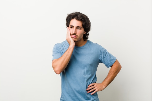 Joven guapo contra una pared blanca que está aburrido, cansado y necesita un día de relax.