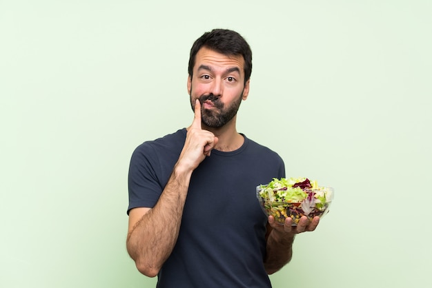 Joven guapo con ensalada sobre pared verde aislado mirando hacia adelante