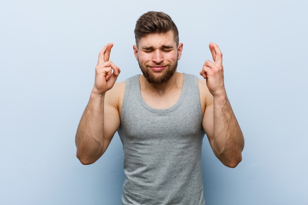 Foto joven guapo fitness cruzando los dedos para tener suerte