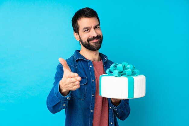 Joven guapo con un gran pastel sobre azul estrechándole la mano para cerrar un buen negocio