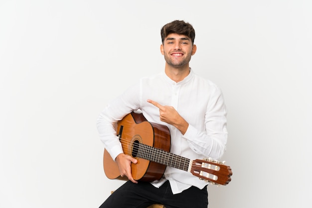 Joven guapo con guitarra sobre blanco aislado apuntando hacia el lado para presentar un producto