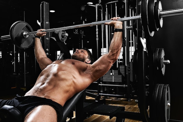 Joven guapo haciendo ejercicio de prensa de banco en el gimnasio fitness motivación deportes estilo de vida salud