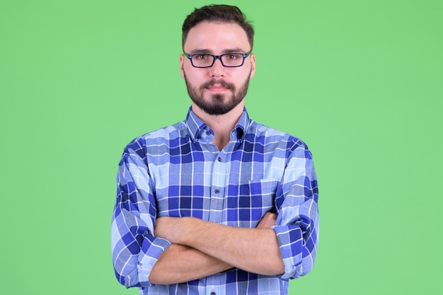 Joven guapo hipster barbudo con anteojos contra chroma key con pared verde