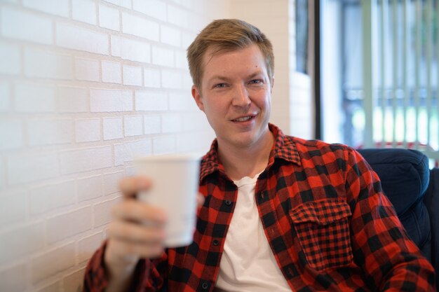 Joven guapo hipster sonriendo mientras sostiene la taza de café