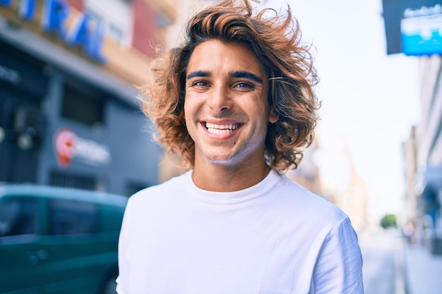 Joven guapo hispano sonriendo feliz caminando en la calle de la ciudad