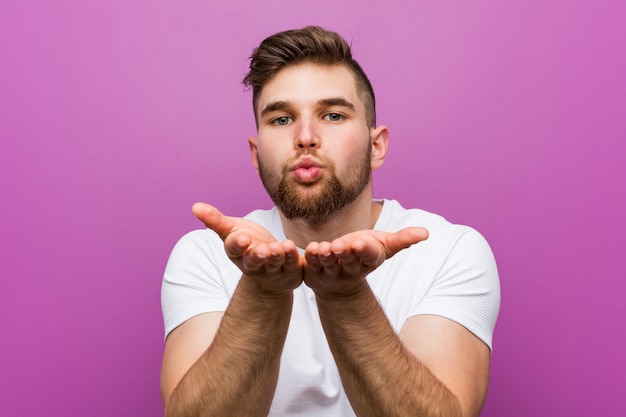 Joven guapo hombre caucásico doblando los labios y sosteniendo las palmas para enviar beso de aire.