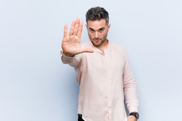 Joven guapo hombre fresco de pie con la mano extendida que muestra la señal de stop, impidiéndole.