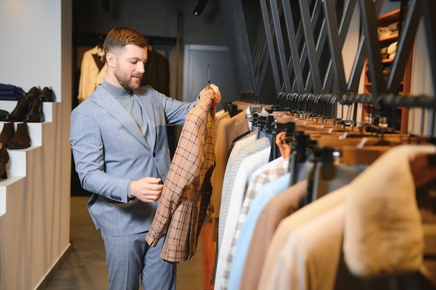 Joven y guapo hombre de negocios moderno buscando y eligiendo un traje clásico en la tienda de trajes