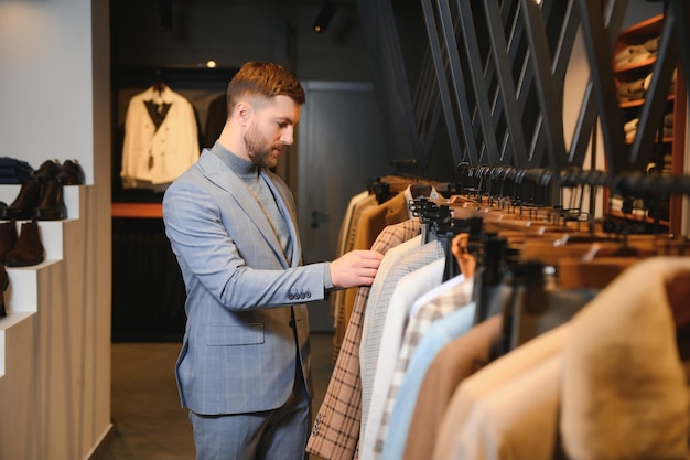 Joven y guapo hombre de negocios moderno buscando y eligiendo un traje clásico en la tienda de trajes