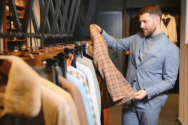 Joven y guapo hombre de negocios moderno buscando y eligiendo un traje clásico en la tienda de trajes