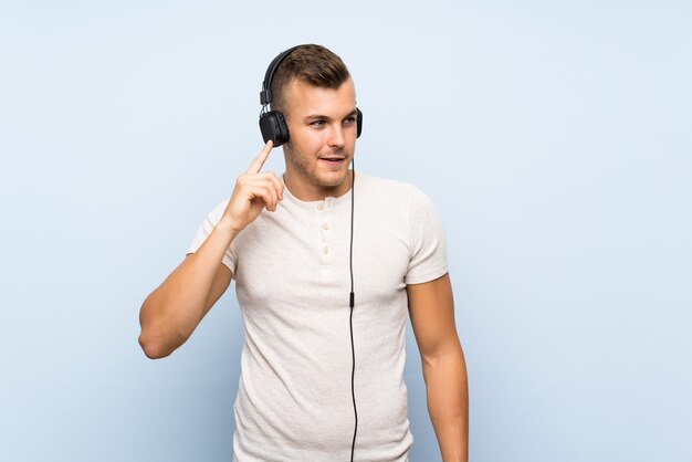 Joven guapo hombre rubio sobre fondo azul aislado escuchando música con auriculares