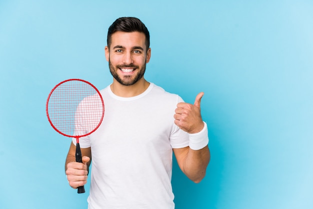 Joven guapo jugando bádminton aislado sonriendo y levantando el pulgar hacia arriba