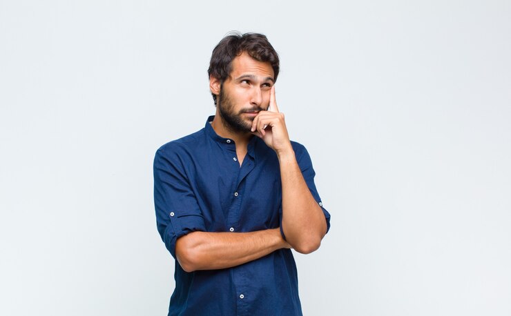 Foto joven guapo latino con una mirada concentrada, preguntándose con una expresión dudosa, mirando hacia arriba y hacia un lado