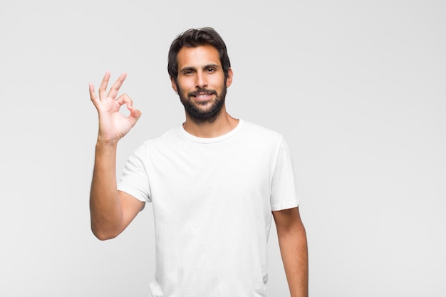 Joven guapo latino que se siente feliz, relajado y satisfecho, mostrando aprobación con gesto bien, sonriendo