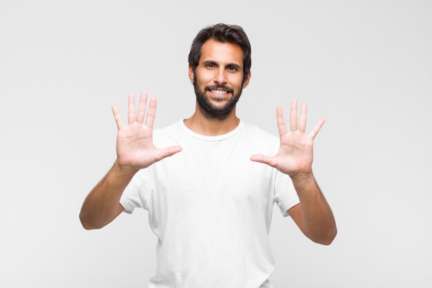 Joven guapo latino sonriendo y mirando amigablemente, mostrando el número diez o décimo con la mano hacia adelante, contando hacia atrás