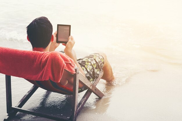 joven guapo leyendo el lector electrónico en la playa