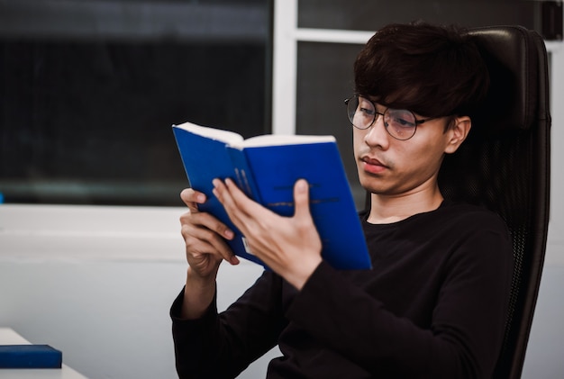 Joven guapo libro de lectura del hombre asiático en el escritorio de trabajo a altas horas de la noche, el conocimiento y el concepto de aprendizaje