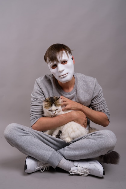 Joven guapo con máscara blanca sobre fondo gris