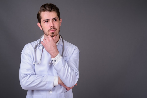 Joven guapo médico barbudo contra la pared gris