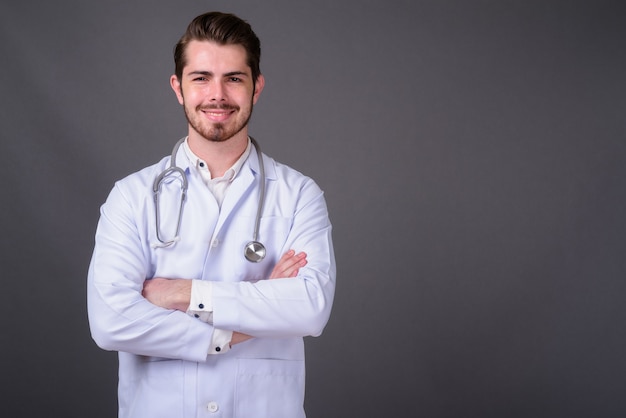 Joven guapo médico barbudo contra la pared gris