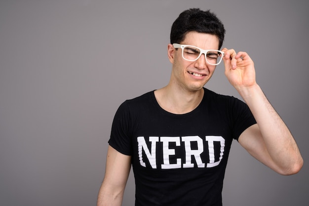 Joven guapo nerd con anteojos contra gris