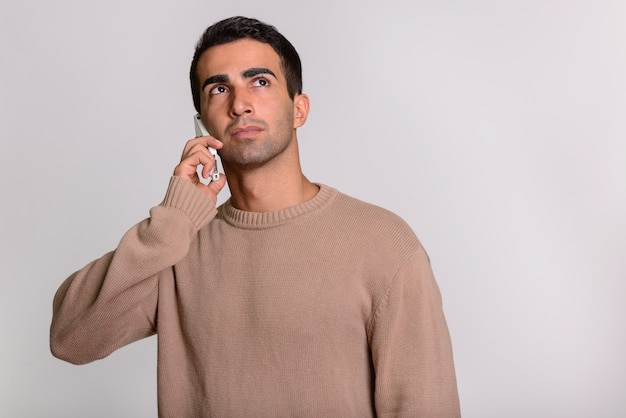 Joven guapo persa hablando por teléfono mientras piensa