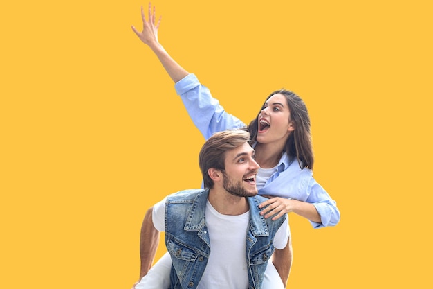 Un joven guapo que lleva a una mujer joven y atractiva en los hombros mientras pasan tiempo juntos en un fondo amarillo