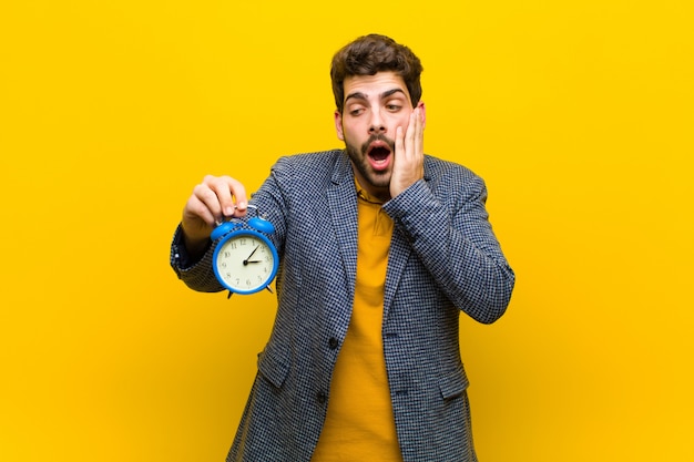 Joven guapo con un reloj de alarma contra naranja