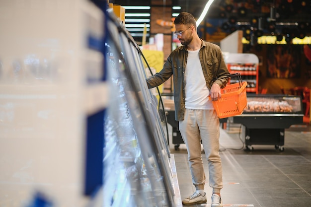 Joven guapo revisa los refrigeradores para la comida congelada en el supermercado