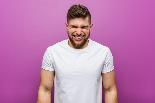 Joven guapo se ríe y cierra los ojos, se siente relajado y feliz