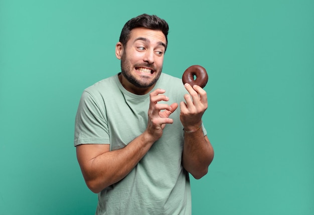 Joven guapo rubio con una dona de chocolate. concepto de desayuno