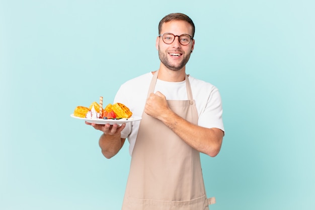 Joven guapo rubio sintiéndose feliz y enfrentando un desafío o celebrando. concepto de gofres de cocina