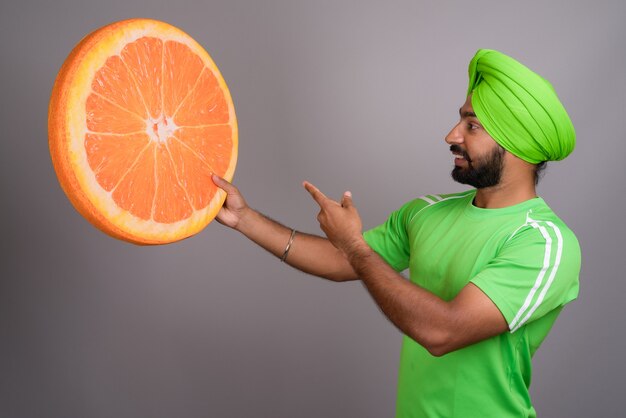 Joven guapo sij indio sosteniendo una gran rodaja de naranja