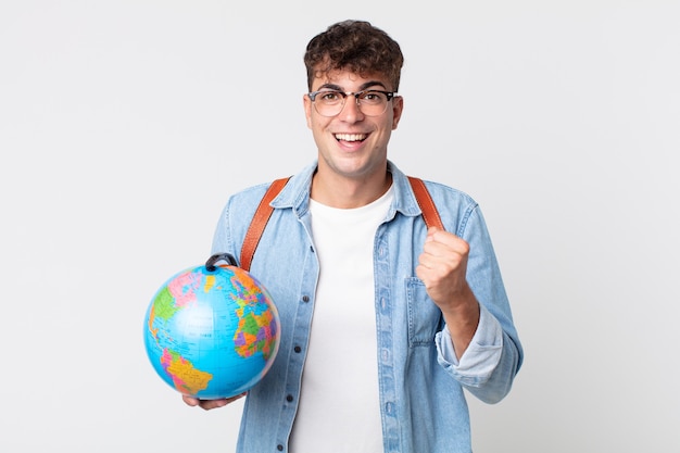 joven guapo sintiéndose conmocionado, riendo y celebrando el éxito. estudiante sosteniendo un mapa del globo terráqueo