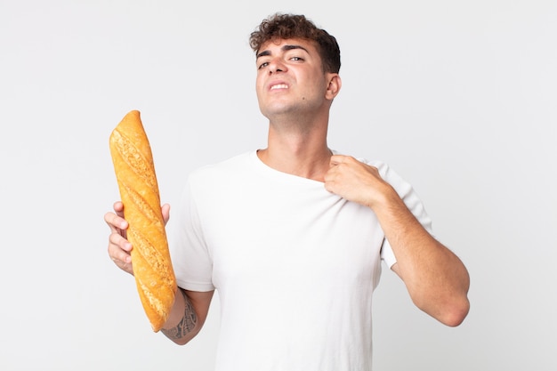 Joven guapo sintiéndose estresado, ansioso, cansado y frustrado y sosteniendo una baguette de pan