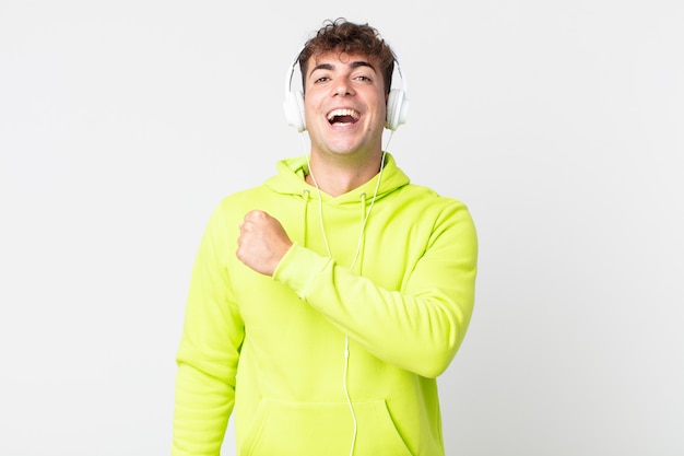 Joven guapo sintiéndose feliz y enfrentando un desafío o celebrando y auriculares