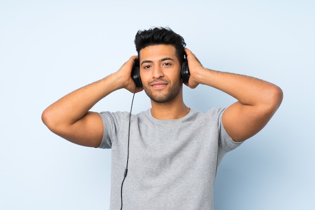 Joven guapo sobre pared aislada usando el móvil con auriculares