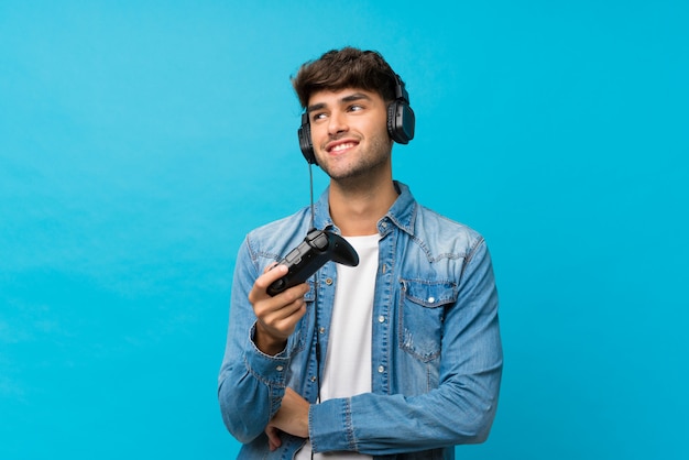 Joven guapo sobre pared azul aislado jugando en videojuegos